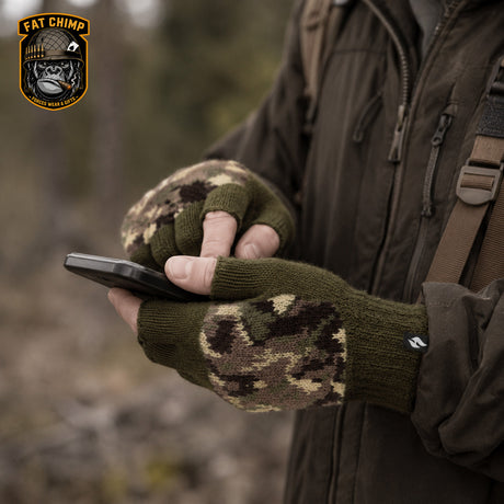 A person outdoors wearing olive green fingerless knit gloves with a brown and beige digital camouflage pattern on the palms and wrists, holding a smartphone. A 'Fat Chimp' brand logo is visible in the top-left corner.