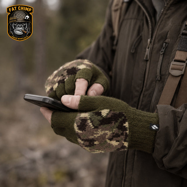 A person outdoors wearing olive green fingerless knit gloves with a brown and beige digital camouflage pattern on the palms and wrists, holding a smartphone. A 'Fat Chimp' brand logo is visible in the top-left corner.