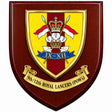 A shield-shaped wooden plaque with a polished dark reddish-brown wood finish, featuring a gold-bordered crest with a yellow, red, white, and blue design, and a gold scroll reading '9th/12th Royal Lancers (POWs)'.