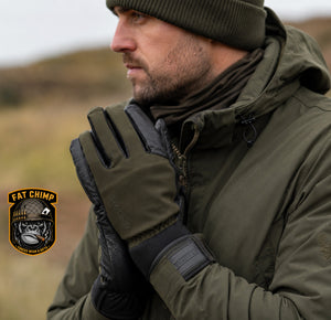 A man wearing an olive green hooded jacket, matching beanie, and black-and-olive gloves stands outdoors in a blurred natural setting. A 'Fat Chimp' brand patch is visible in the lower-left corner.