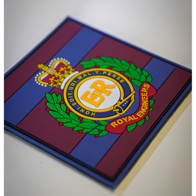 A square glass or acrylic coaster featuring the Royal Engineers crest, set against a background of blue and maroon stripes. The crest is detailed with gold, green, and red elements.
