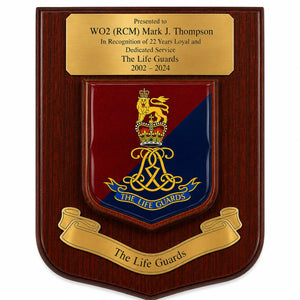 A wooden commemorative plaque with a polished gold-tone top inscription plate and a central shield featuring the Life Guards crest in red and blue with gold detailing, plus a gold scroll reading 'The Life Guards' at the bottom.