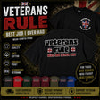 A promotional product graphic for a black graphic T-shirt featuring the words 'veterans rule' and 'BEST JOB I EVER HAD' with small Union Jack flags. The image shows two views of the shirt, large marketing text, feature callouts, a circular badge, and a row of other shirt color options along the bottom on a dark textured background.