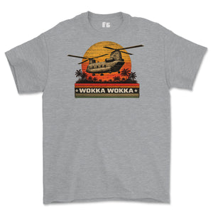 A heather gray short-sleeve t-shirt featuring a retro graphic of a military CH-47 helicopter flying over a sunset with palm trees and the text 'WOKKA WOKKA'.