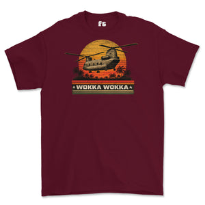 A maroon short-sleeve crewneck t-shirt featuring a retro graphic of a military CH-47 helicopter flying over a sunset with palm trees and the text 'WOKKA WOKKA'.