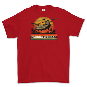 A red short-sleeve crewneck t-shirt featuring a retro graphic of a military helicopter flying over a sunset with palm trees and the text 'WOKKA WOKKA' on a black banner.